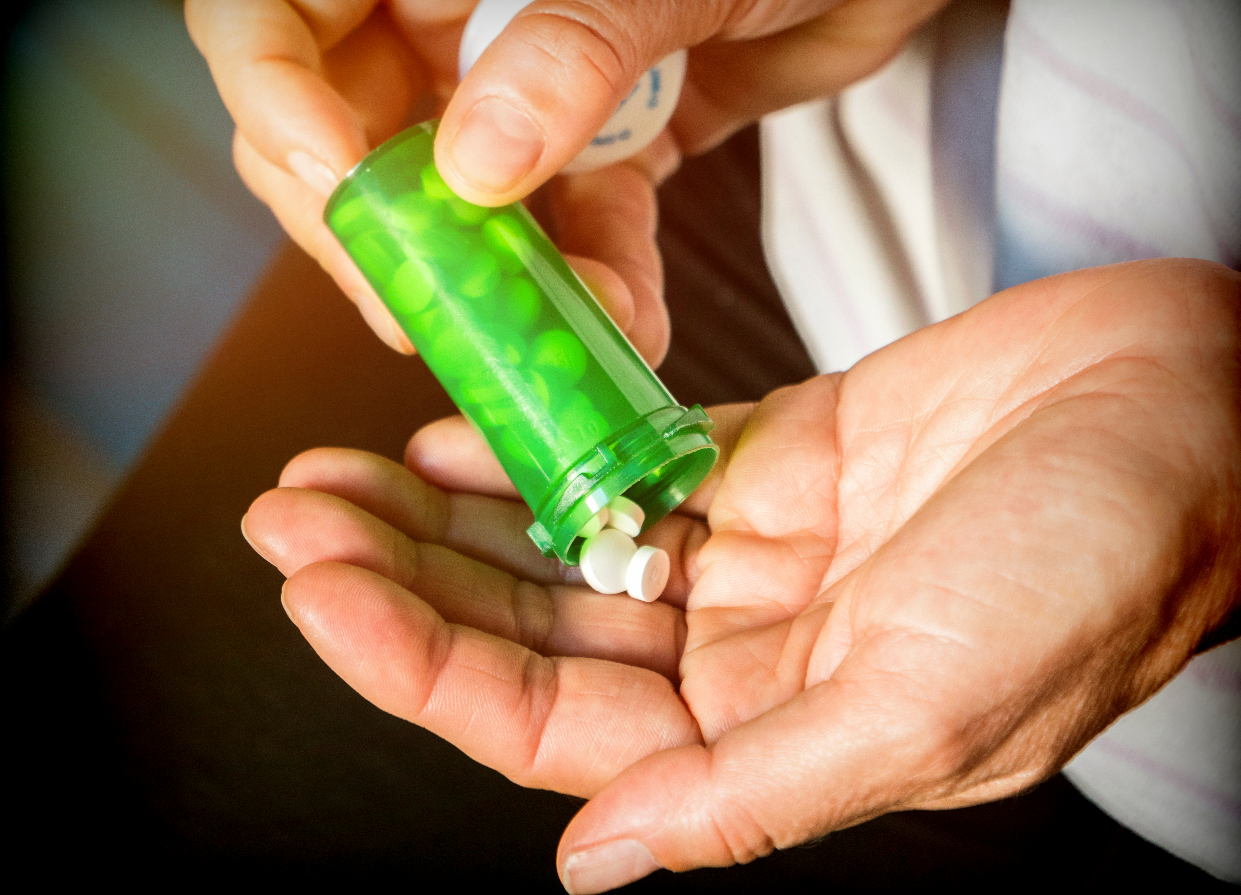 White pills pouring into a hand from a green pill bottle. 